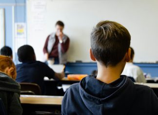 Ethik statt Religion – auch schon für Grundschulen Ein Kind im Vordergrund, welches man von hinten sieht und im Hintergrund ein Lehrer vor einer Tafel. Die GEW möchte, dass Alternativen zum Religionsunterricht ab der ersten Klasse schon angeboten werden.
