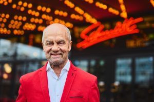 Corny Littmann steht vor dem Schmidt-Theater. Er trägt ein weißes Hemd und eine rote Anzugjacke. 