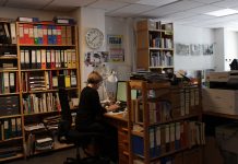 Geschichten aus der Nachbarschaft Eine Frau sitzt an einem Arbeitstisch zwischen vielen Bücherregalen