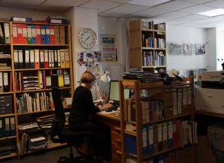 Geschichten aus der Nachbarschaft Eine Frau sitzt an einem Arbeitstisch zwischen vielen Bücherregalen