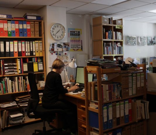 Geschichten aus der Nachbarschaft Eine Frau sitzt an einem Arbeitstisch zwischen vielen Bücherregalen