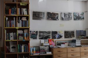 Das Foto zeigt links im Bild ein Bücherregal deckenhoch. Rechts ist ein niedriger Schrank, darüber hängen Fotografien.