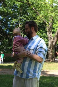 Ein Mann steht in einem grünen Park mit einem Baby auf dem Arm.