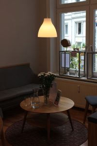 Das Bild zeigt einen kleinen runden Tisch vor einem Sofa. Über dem Tisch hängt eine Lampe.