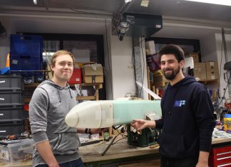Wettbewerb über den Wolken Vor einer Wand voller Geräte und Schubladenschränke stehen Chris Lucas Siewert und Fabian Fabian Kühn, zwei Mitglieder des Vereins Neues Fliegen, mit einem Modellflugzeug.