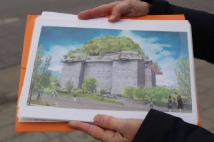 Zwei Hände halten ein Foto in DinA4. Das Foto ist eine Visualisierung des Bunkers an der Feldstraße, im Prozess der Begrünungsplanung.