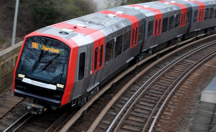 U-Bahn Linie U3 mit der Aufschrift Barmbek fährt auf einem Gleis, Hintergrund leicht verschwommen.