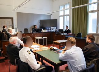 Schuldig: Urteil gegen Hamburger Polizisten In einem Gerichtsaal sitzen Personen an Tischen zueinander, wobei drei Gesichter zesniert sind.