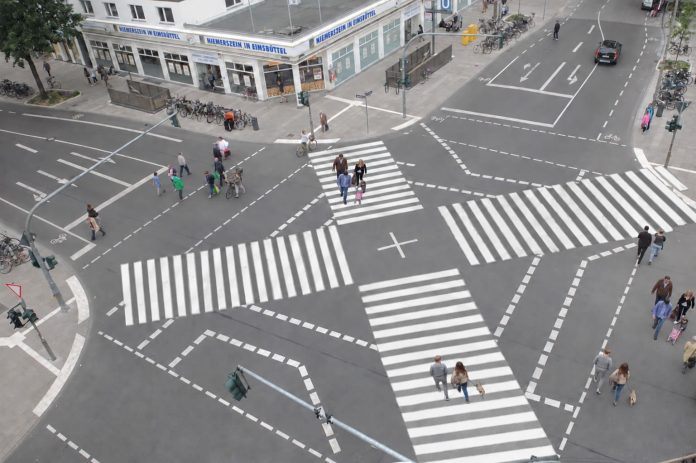 Eine Kreuzung ist von oben zu sehen. Auf dem Aspahlt befinden sich Zebrastreifen, die sich wie ein Kreuz in der Mitte überschneiden.