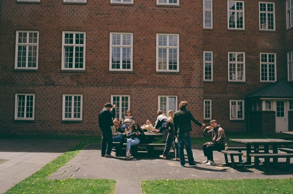Die Finken am Campus Finkenau. Foto: Rosa Bort Mehrere Menschen stehen vor einem roten Backsteinhaus und sitzen um einen Holztisch.