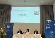 Kooperation zwischen DESY und HAW: Pläne für die nächsten Jahre vorgestellt Auf einer Bühne der HAW Hamburg sitzen drei Personen, die den Kooperationsvertrag umherreichen.