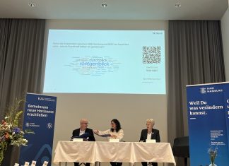 Kooperation zwischen DESY und HAW: Pläne für die nächsten Jahre vorgestellt Auf einer Bühne der HAW Hamburg sitzen drei Personen, die den Kooperationsvertrag umherreichen.